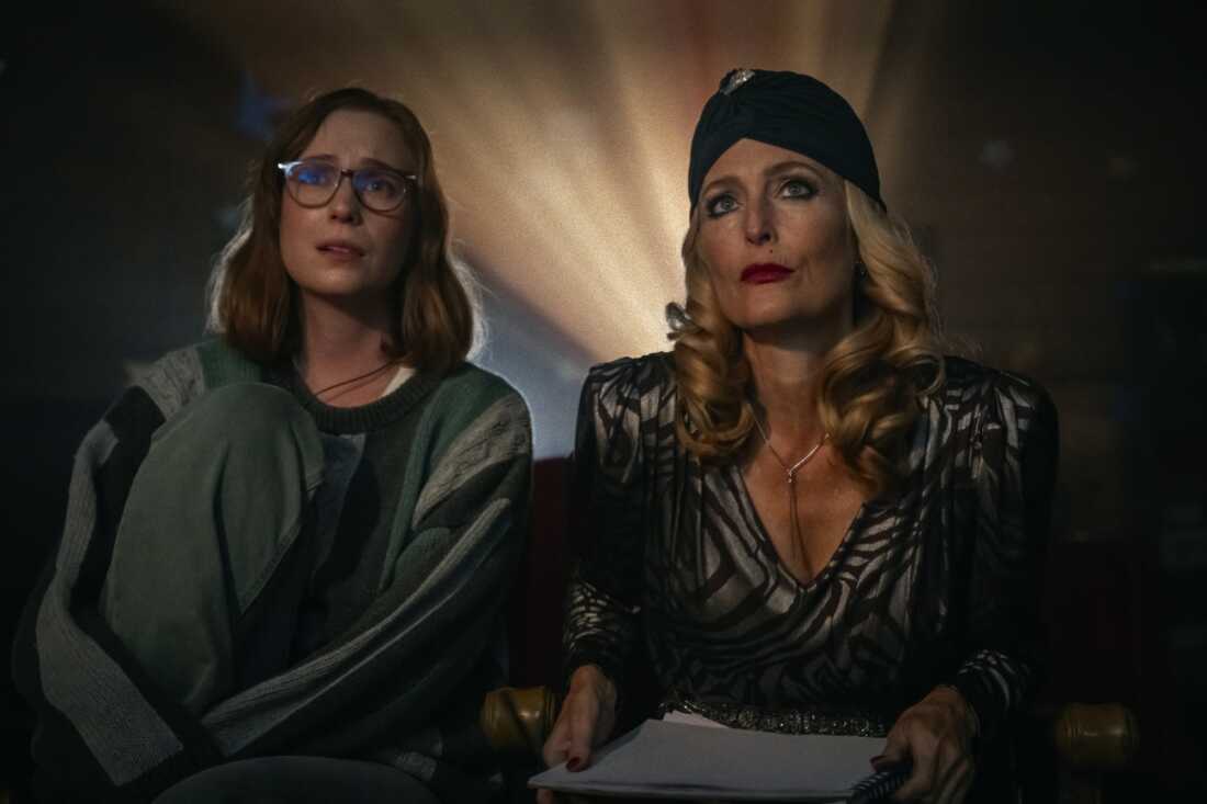 Film still of two women sitting looking forward with a movie camera light behind them.