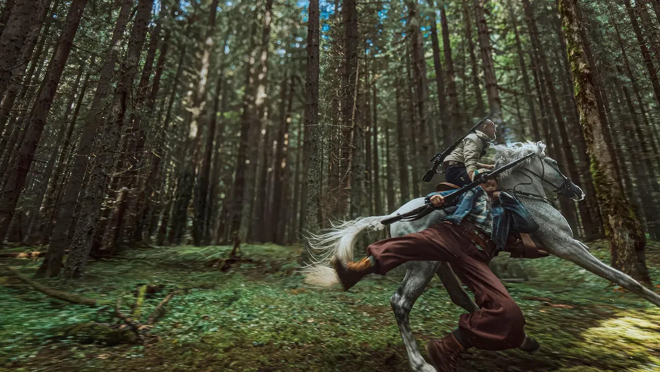 Film still of a person on horseback through a forest.