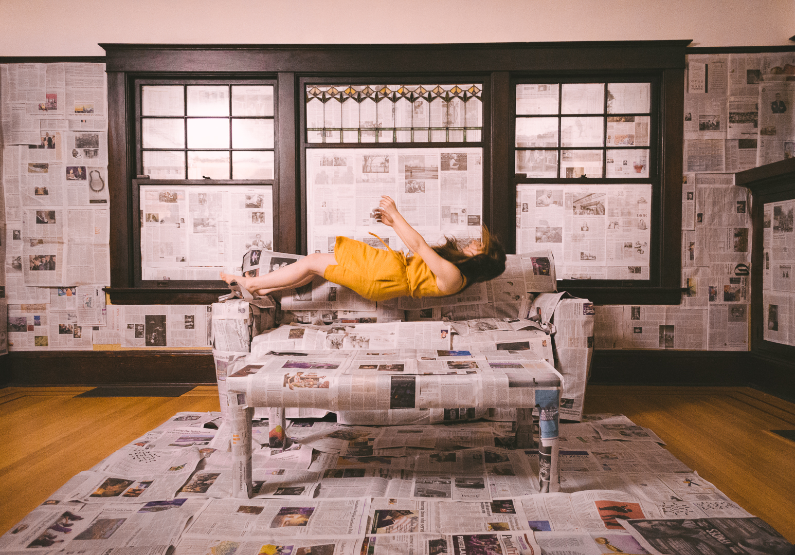 Film still of a person levitating above a couch that is covered with newspapers, in a room covered in newspapers.