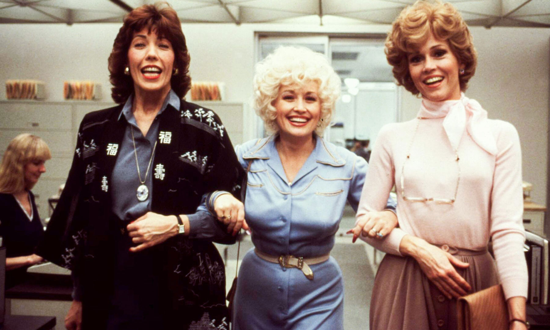 Film still of three women in an office with their arms linked