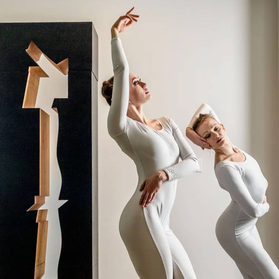 Two dancers next to a sculpture.