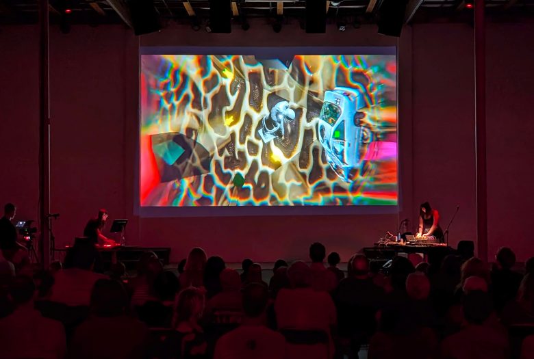 Photo of two artists at the sides of a screen with psychedelic imagery on it.