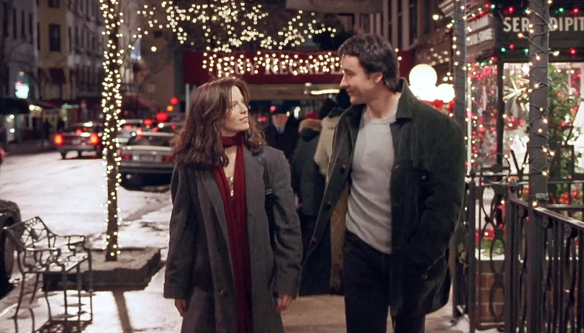 Film still from Serendipity, where a man and a woman on a city street at night are looking at each other.