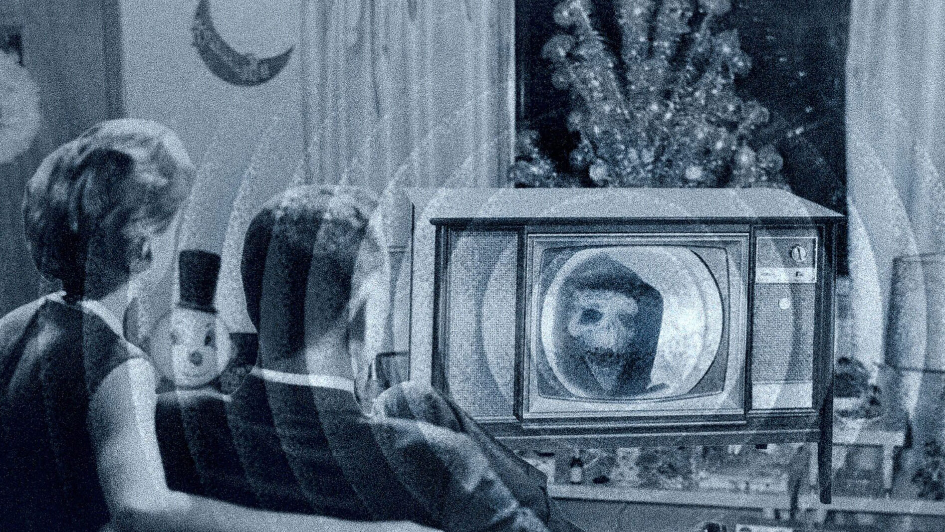 Old black and white photo of a man and women watching a TV with a ghostly figure on it.