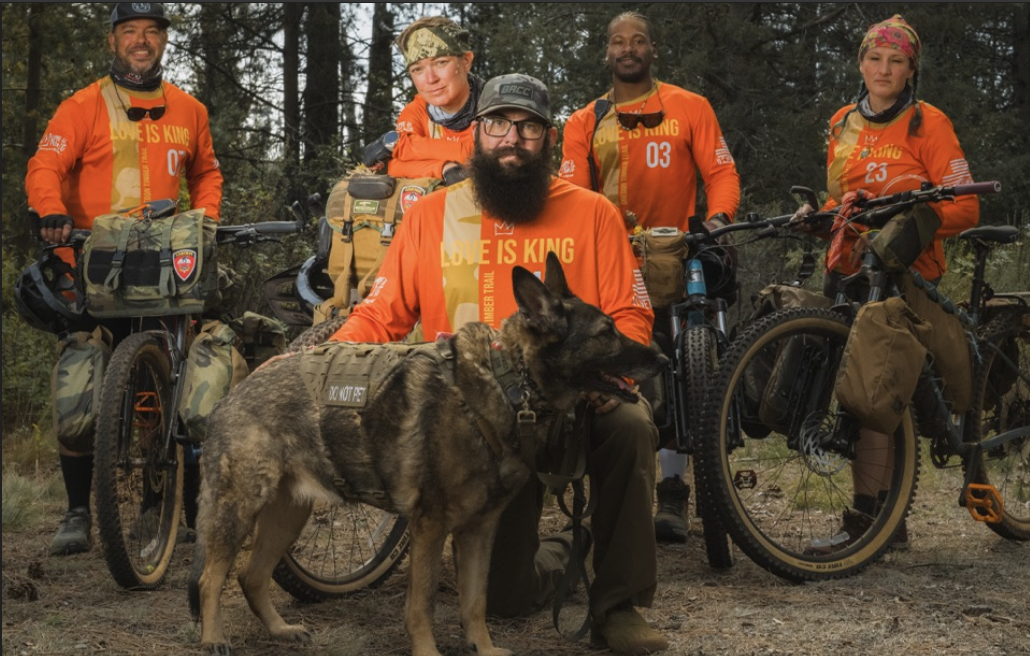 A group of people in orange shirts, some with bikes, and one in front with a dog.