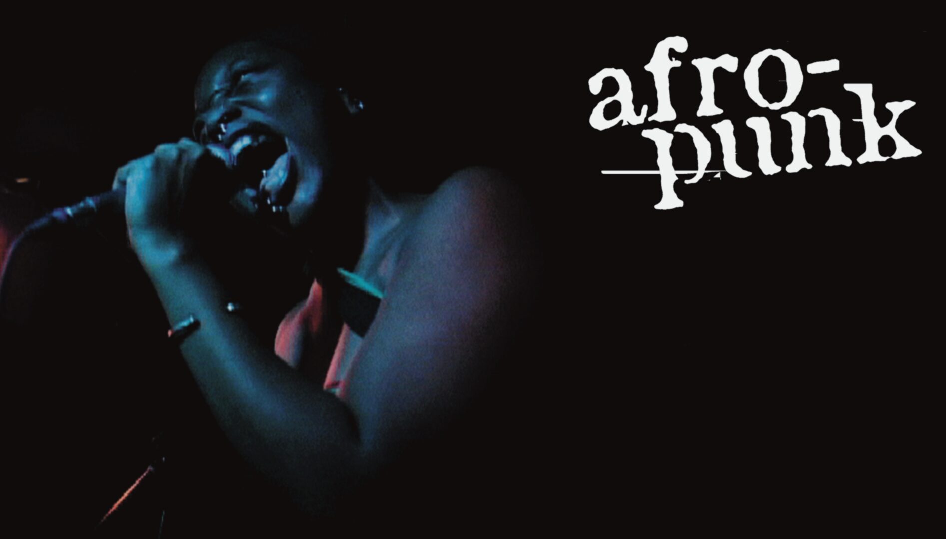 Film still of a Black woman singing into a microphone. The word afro-punk is in the top right corner of the image.